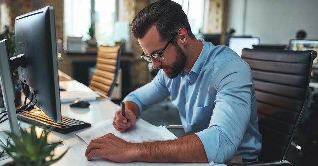 Busy architect. Young andsuccessfulbearded man in eyeglasses and formal wear drawing something while working in the office. Engineer. Construction plan