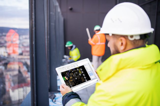 Mature man engineer standing on construction site, holding tablet with blueprints.